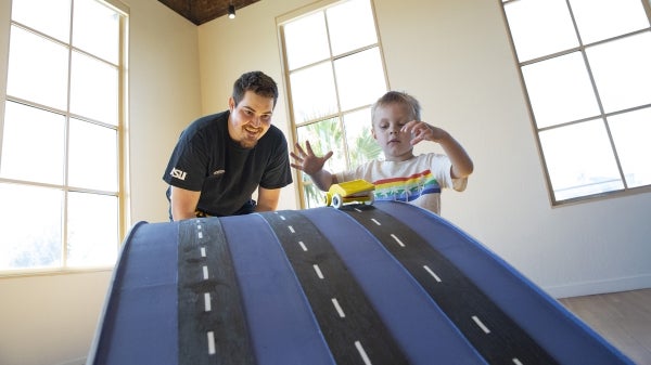 A man and child watch a toy car go down a ramp