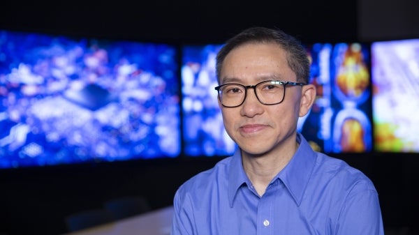 Baoxin Li with monitors that display images of microchips and MRIs behind him.